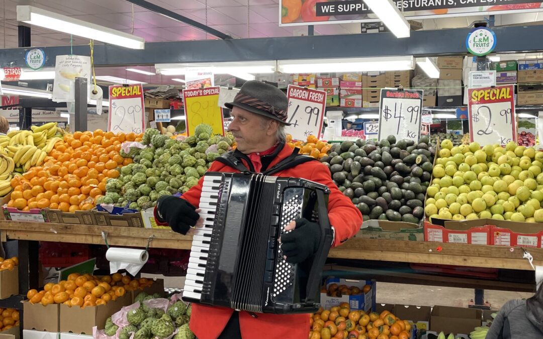 Man playing accordion in front of fruit stand
