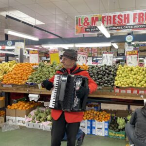 Man playing accordion in front of fruit stand