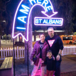 Woman, man & child standing near neon light art installation